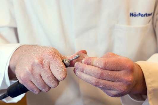 Ein Hörakustiker schleift ein Hörgerät mit einem Fräsgerät in einer Werkstatt.